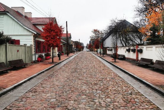 Zdjęcie "Jesień w Mieście Tkaczy" przedstawia brukowaną ulicę oraz zabytkową drewnianą zabudowę Parku Kulturowego Miasto Tkaczy w Zgierzu. 