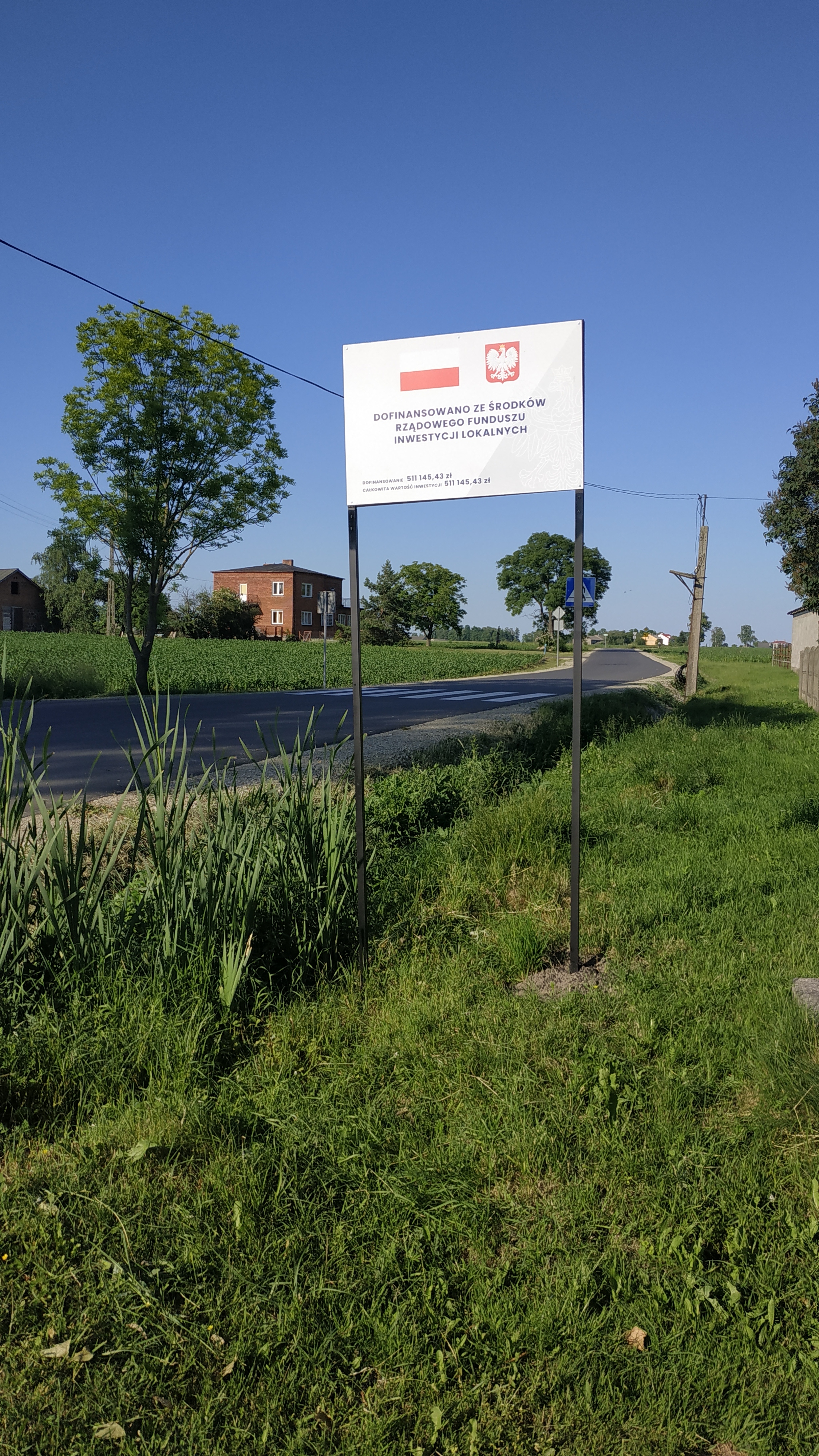Zdjęcie przedstawia drogę wraz z tablicą informacyjną od strony m. Popów Głowieński
